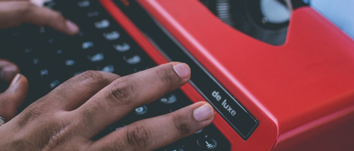 A person typing on a red typewriter.